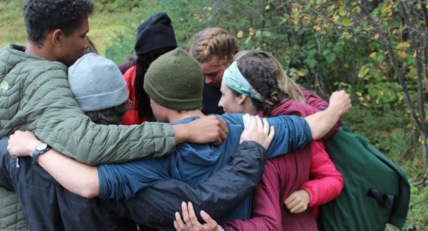 A group of students huddle in a circle with their arms around one another. 